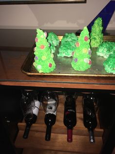 a cake with green frosting in the shape of trees on a tray next to bottles of wine