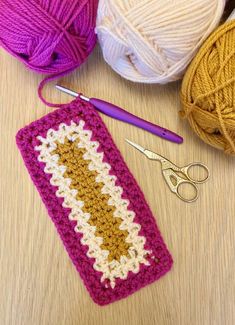 a crochet bag next to some yarn and scissors on a table with balls of yarn