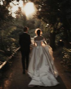 a bride and groom walking down a path in the woods at sunset or sunrise time