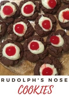 chocolate cookies with white frosting and red cherries on top, sitting on a wooden cutting board