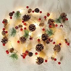 christmas lights and pine cones are arranged in the shape of a circle on a white surface