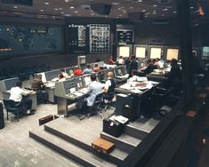 a control room filled with lots of people sitting at desks in front of monitors