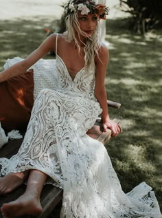 a woman sitting on top of a wooden bench wearing a white dress and flower crown