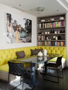 a yellow couch sitting in front of a book shelf next to a table with chairs