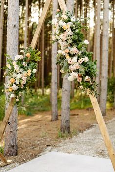 an arch decorated with flowers and greenery stands in front of the trees at this outdoor ceremony