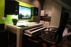 a desk with a keyboard, monitor and speakers on it in a room that has green walls