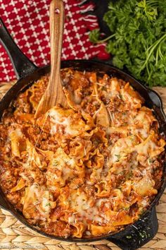 a skillet filled with pasta and sauce on top of a woven place mat next to parsley