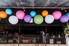 colorful paper lanterns are hanging from the ceiling in front of an outdoor venue with tables and chairs