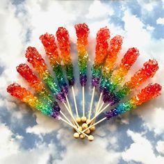 a bunch of candy sticks sitting on top of a cloud filled sky with rainbow colored candies