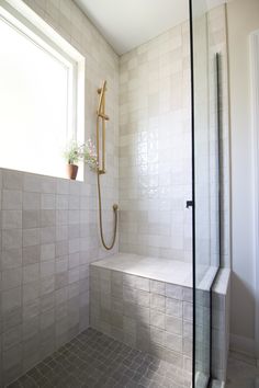 a white tiled bathroom with a shower and window