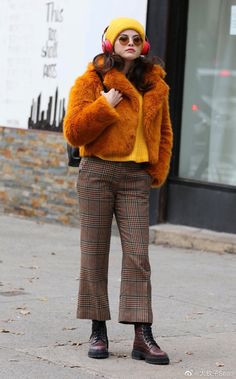 a woman wearing headphones and a fur coat is standing on the sidewalk in front of a store