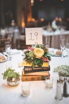 a table topped with lots of books covered in flowers and greenery next to candles