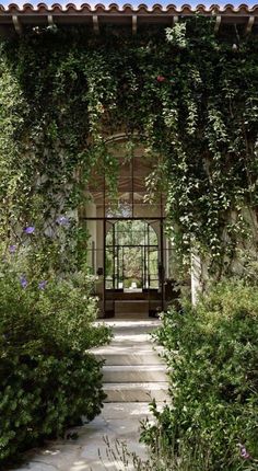 an entrance to a house covered in vines and flowers with a bench on the other side