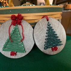 two christmas tree ornaments sitting on top of a green cloth covered tablecloth next to a basket