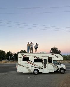 three people standing on top of an rv parked in the middle of a parking lot