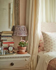 a bed room with a lamp a mirror and some books on the nightstand next to it