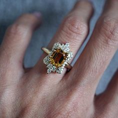 a close up of a person's hand wearing a ring with an orange and white diamond