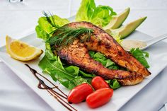 a white plate topped with chicken, lettuce and tomatoes next to lemon wedges