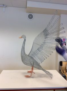 a sculpture of a bird made out of wire sitting on top of a white table