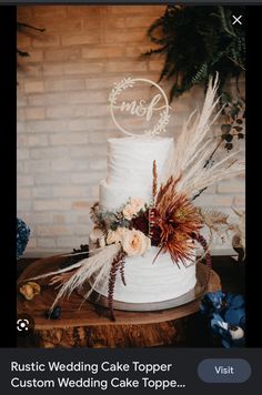 a white wedding cake topped with flowers and feathers on top of a wooden table next to a brick wall