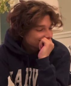 a young man with curly hair is eating something while wearing a hoodie and looking at the camera