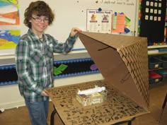 a young boy holding up an umbrella made out of cardboard in front of a table