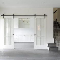 an empty living room with white walls and open closet doors on the wall, along with stairs leading up to two sets of bookshelves