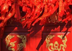 two red doors with gold designs on them and ribbons hanging from the top to the bottom