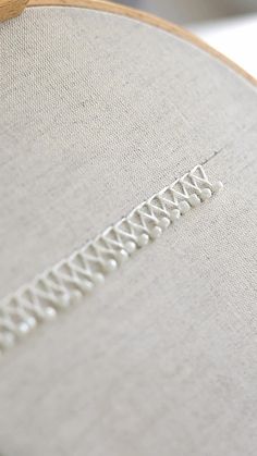 a close up view of a cross stitched pattern on a white fabric with a wooden hoop in the foreground