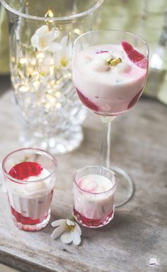 two glasses filled with different types of desserts on a wooden table next to flowers