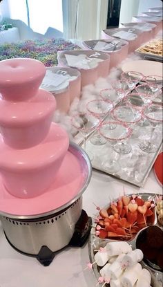 there are many bowls and trays of food on the table with pink frosting