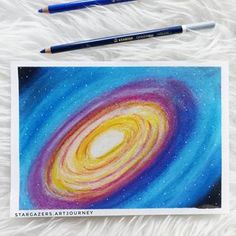 a drawing of a spiral galaxy with two colored pencils next to it on a fluffy white surface