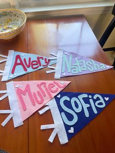 three pennants with name on them sitting on top of a wooden table next to a bowl