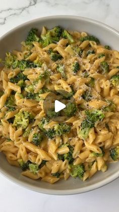 a bowl filled with pasta and broccoli on top of a marble countertop