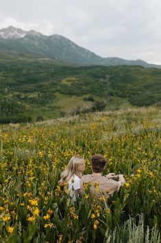 a man and woman are sitting in the middle of a field full of wildflowers