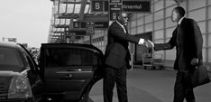 two men in suits shaking hands next to cars