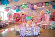 a room filled with lots of tables covered in balloons and paper decorations on the ceiling