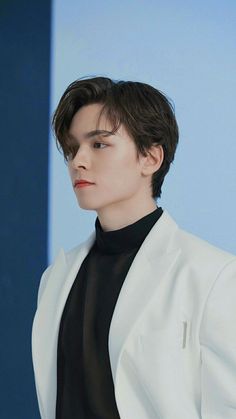 a young man in a white suit and black turtle neck shirt looking off to the side