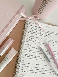 a pink notebook and pen sitting on top of a table next to an empty cup