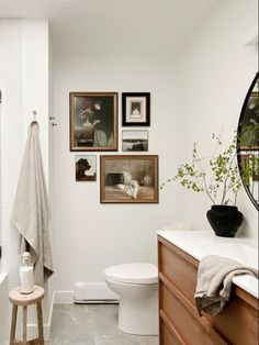 a white bathroom with pictures on the wall and a stool in front of the toilet