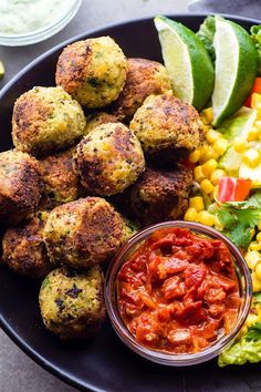 a black plate topped with meatballs, corn and salsa next to lettuce