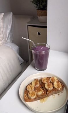 toast with banana slices on it next to a glass of purple liquid and a bed in the background