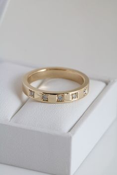 a gold wedding band with five diamonds on it in a white gift box for the bride