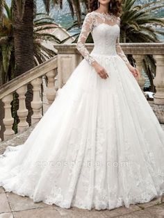 a woman in a white wedding dress standing on stairs with palm trees and water behind her