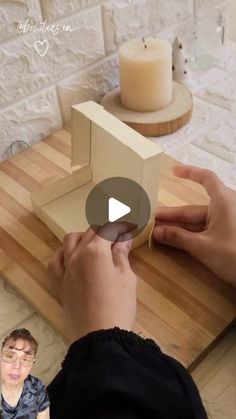 a person is making a cardboard house on a wooden table with a candle in the background