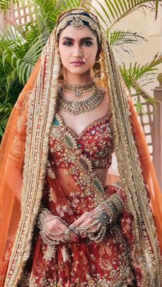 a woman in a red and gold bridal gown with jewelry on her head, standing next