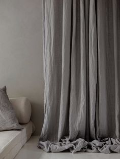 a white couch sitting next to a window covered in gray linens and drapes