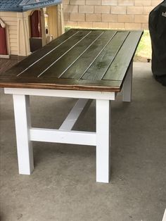 a wooden table sitting on top of a cement floor next to a brick building with a blue roof