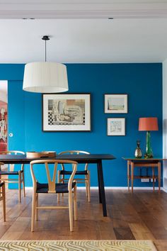 a dining room with blue walls and wooden flooring is pictured in this image, there are several chairs around the table