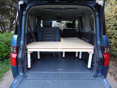 the back end of a blue van with two tables in it's cargo area